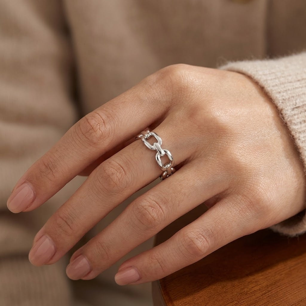 A close-up of a hand wearing a silver chain-link ring, styled with a beige knit sweater against a warm brown wooden surface - J.Collins Jewelry