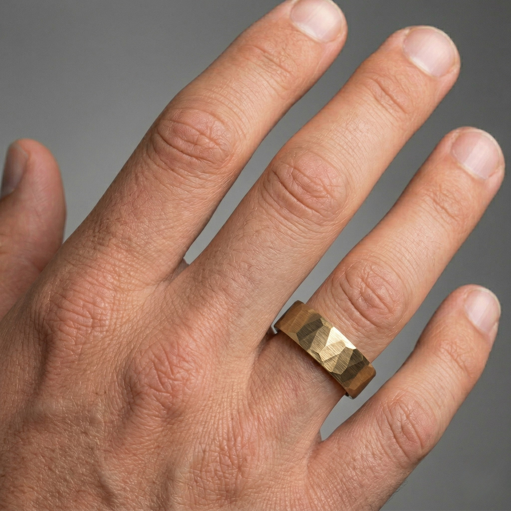 Hand wearing a gold ring on a gray background-J.Collins Jewelry