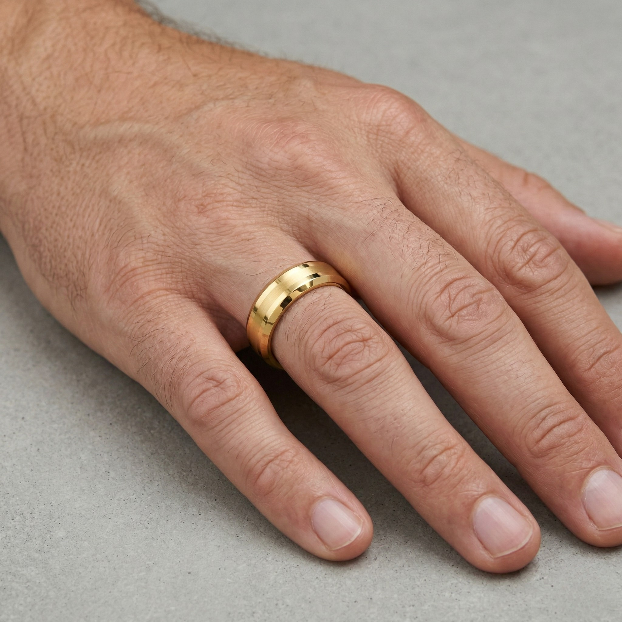 Gold Bevelled Edge Wedding Band Ring with Brushed Centre Worn on Male Hand Against Stone Surface - J. Collins Jewelry 