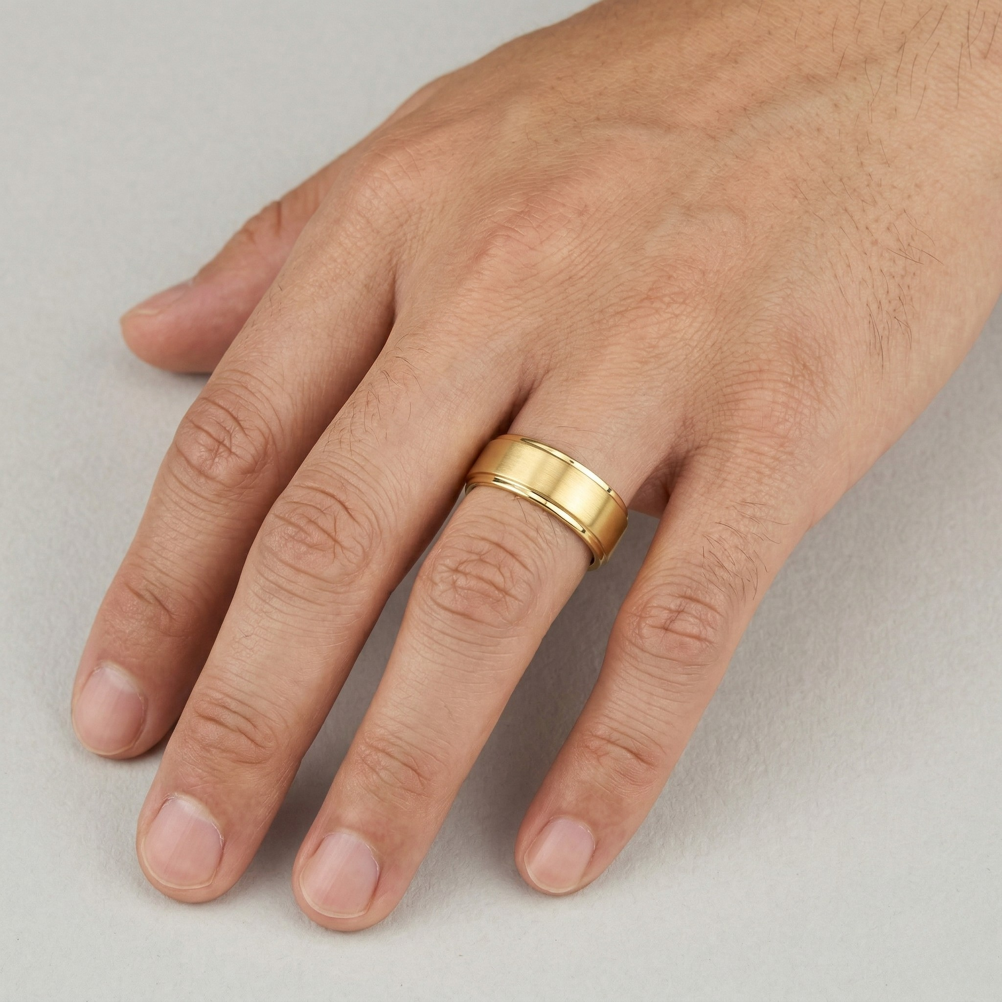 Gold Bevelled Edge Wedding Band Ring with Brushed Centre Worn on Male Hand Against Stone Surface - J. Collins Jewelry 