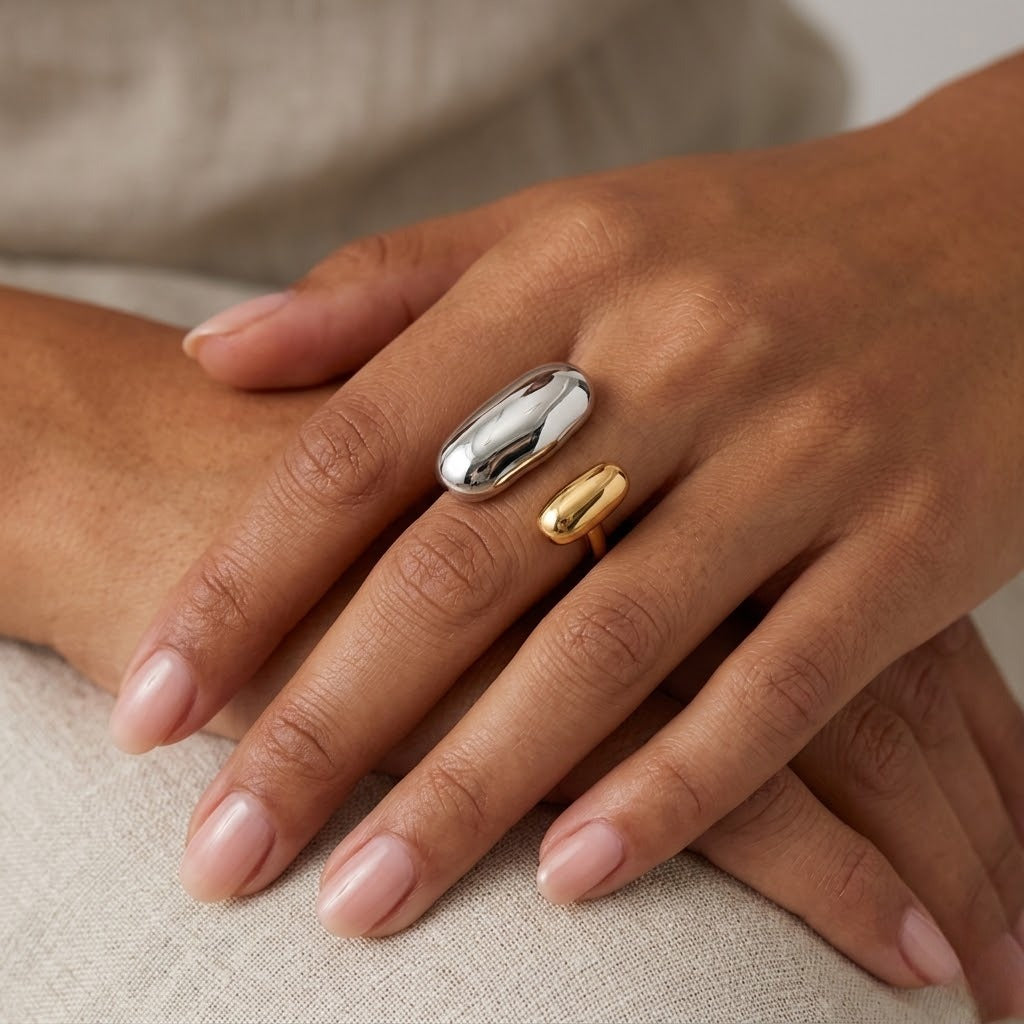 A close-up of a hand wearing two minimalist rings: a larger polished silver dome ring and a smaller gold band ring - JCollins Jewelry