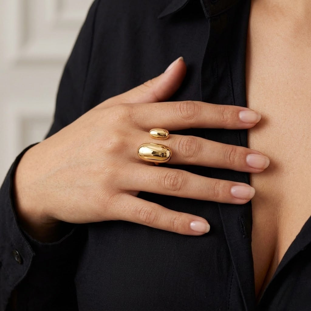 A close-up of a person's hand wearing two polished gold rings, one small and one larger, styled with a black button-down shirt - J.Collins Jewelry