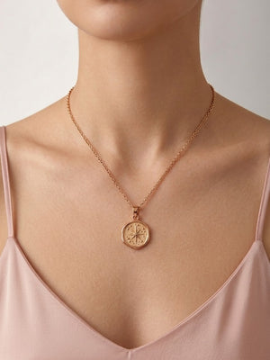 A close-up of a model wearing a delicate rose gold chain necklace with a circular compass pendant, styled with a light pink camisole top against a neutral background - J.Collins Jewelry