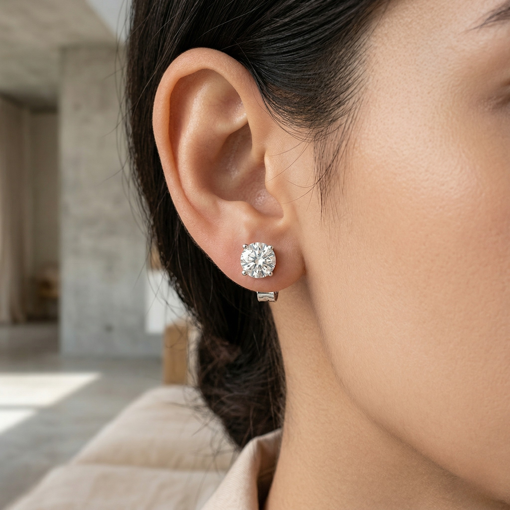 Close-up of a person wearing diamond stud earrings with a blurred indoor backgrounD. - White Gold Diamond Earrings - J. Collins Jewelry 