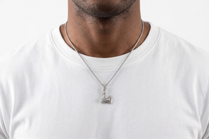 Man wearing a white t-shirt and necklace with a small pendant on a plain background- J.Collins Jewelry