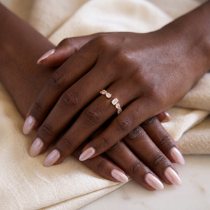 Zircon wrap band in gold on hand with light nude manicure, resting on beige fabric