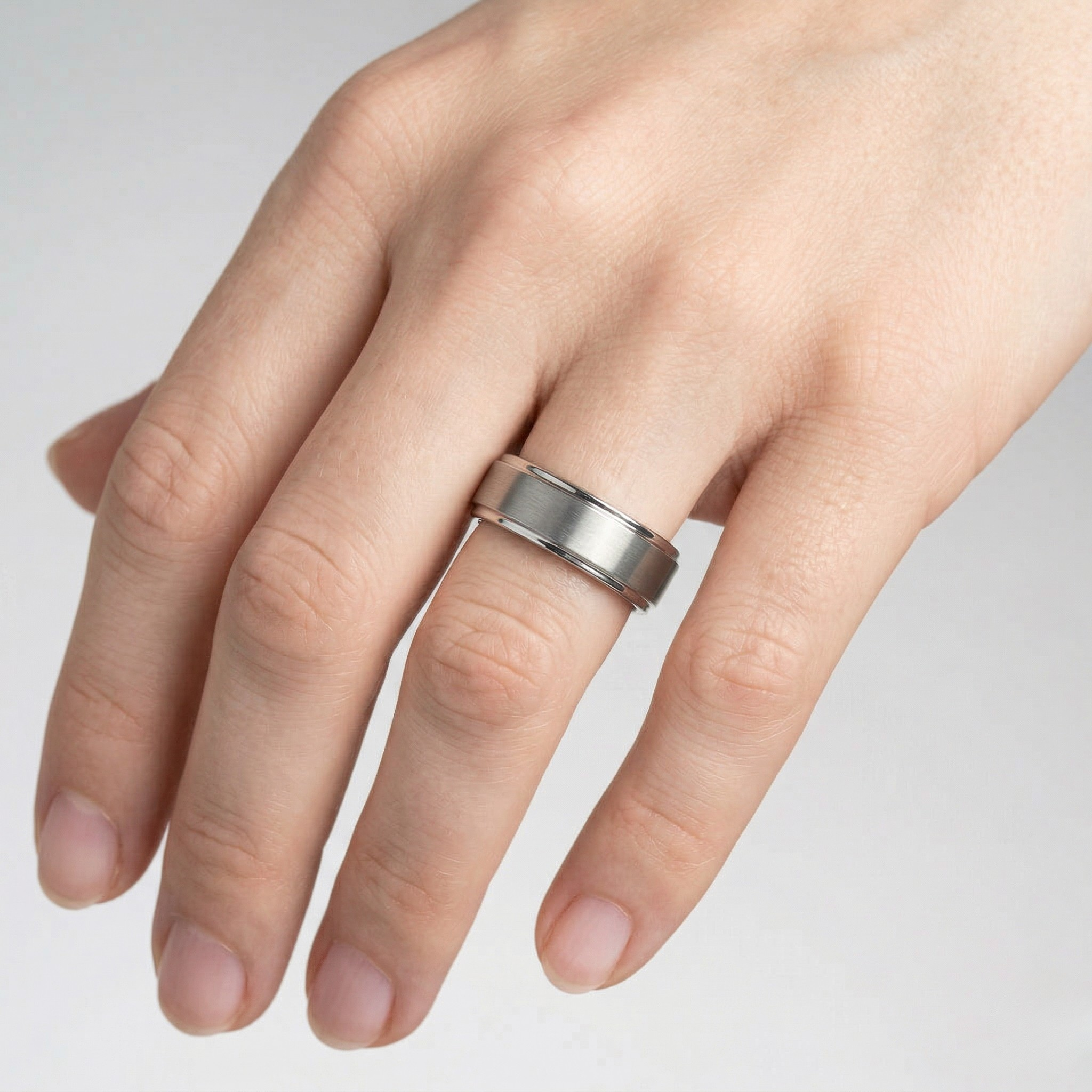 Hand wearing a silver ring on a light gray background