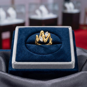 Gold marquise vine ring with two clear stones displayed in a blue velvet box in a jewelry store setting.