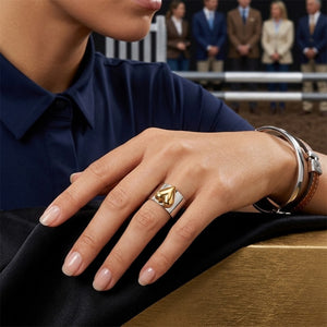 Silver and gold heart accent band on hand, worn with bracelet and watch, background with people blurred.