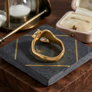 Gold Crested Twin Band ring on slate and wood with hourglass, open velvet box nearby
