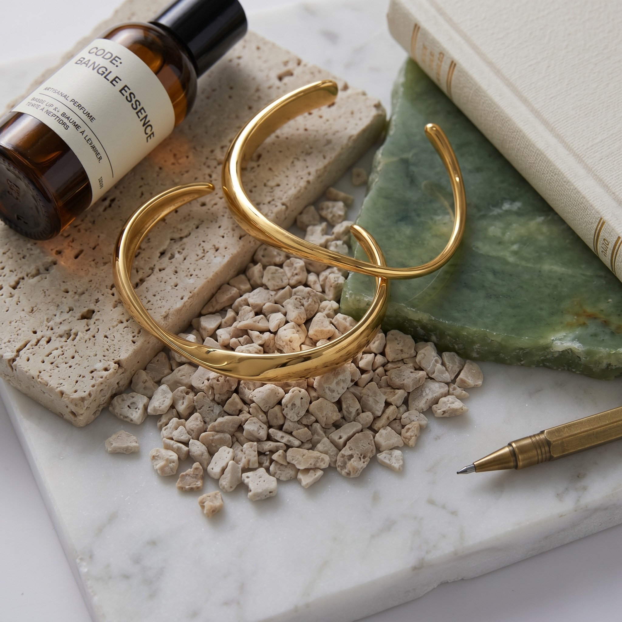 Gold infinity curve bangles on a marble surface with stones, pen, and bottle; elegant and minimalist style.