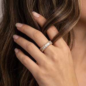 Gold opulent bar ring worn on a woman's finger with long brown hair in lifestyle setting