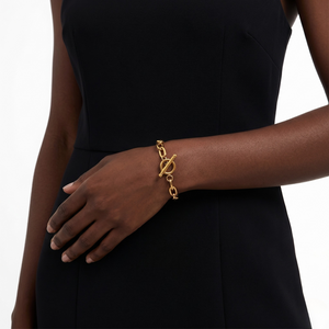 Gold plated charm bangle on model's wrist, wearing a sleeveless black dress