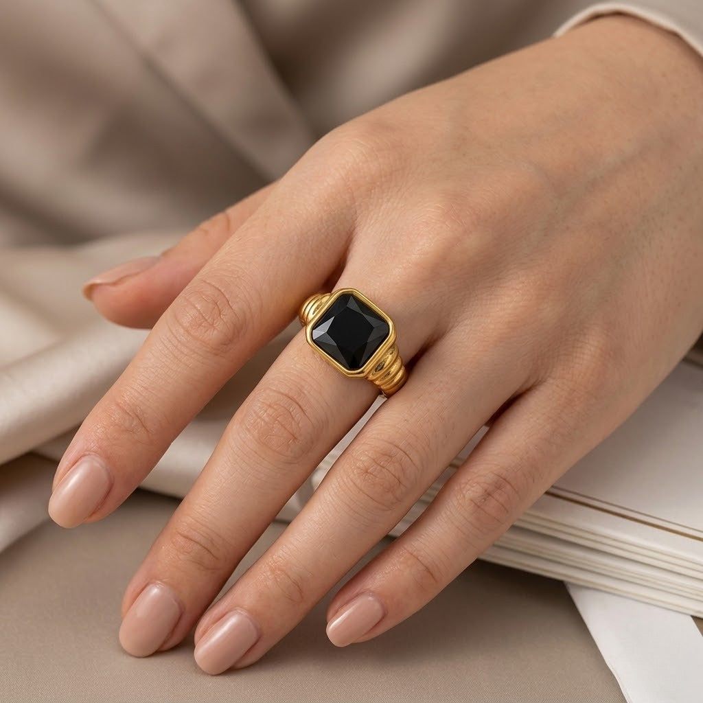 Gold signet ring with black stone on person’s hand, displaying elegant style and craftsmanship.