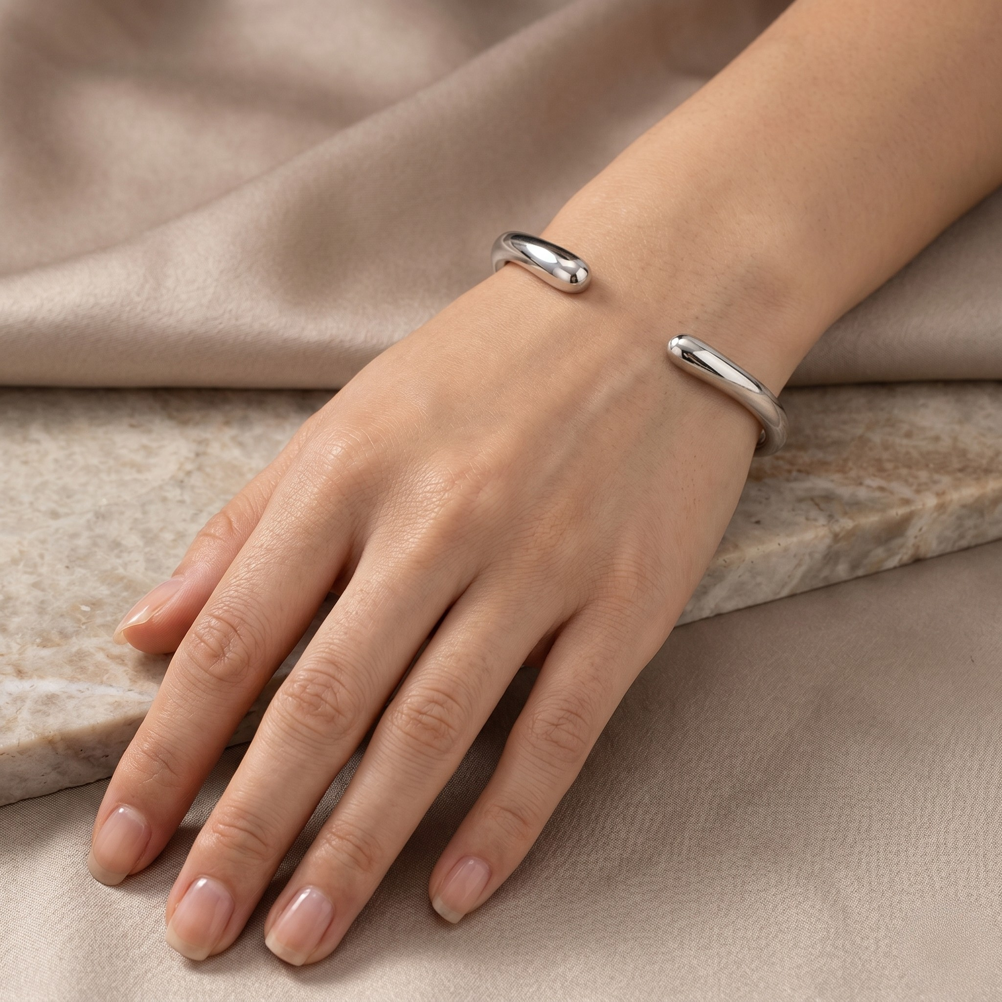 Silver essential cuff pair worn on a hand, displayed on a stone surface.