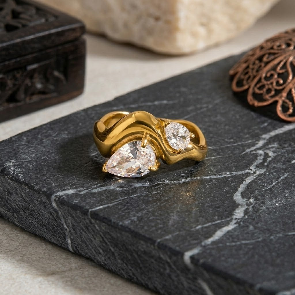 Gold double band ring with pear-shaped and round diamonds on a marble surface