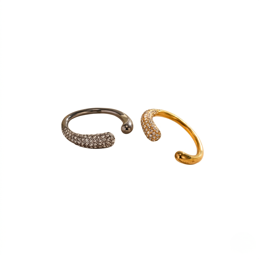 Two curved pavé rings, one gold and one silver with clear stones, showcasing elegant minimalist design.