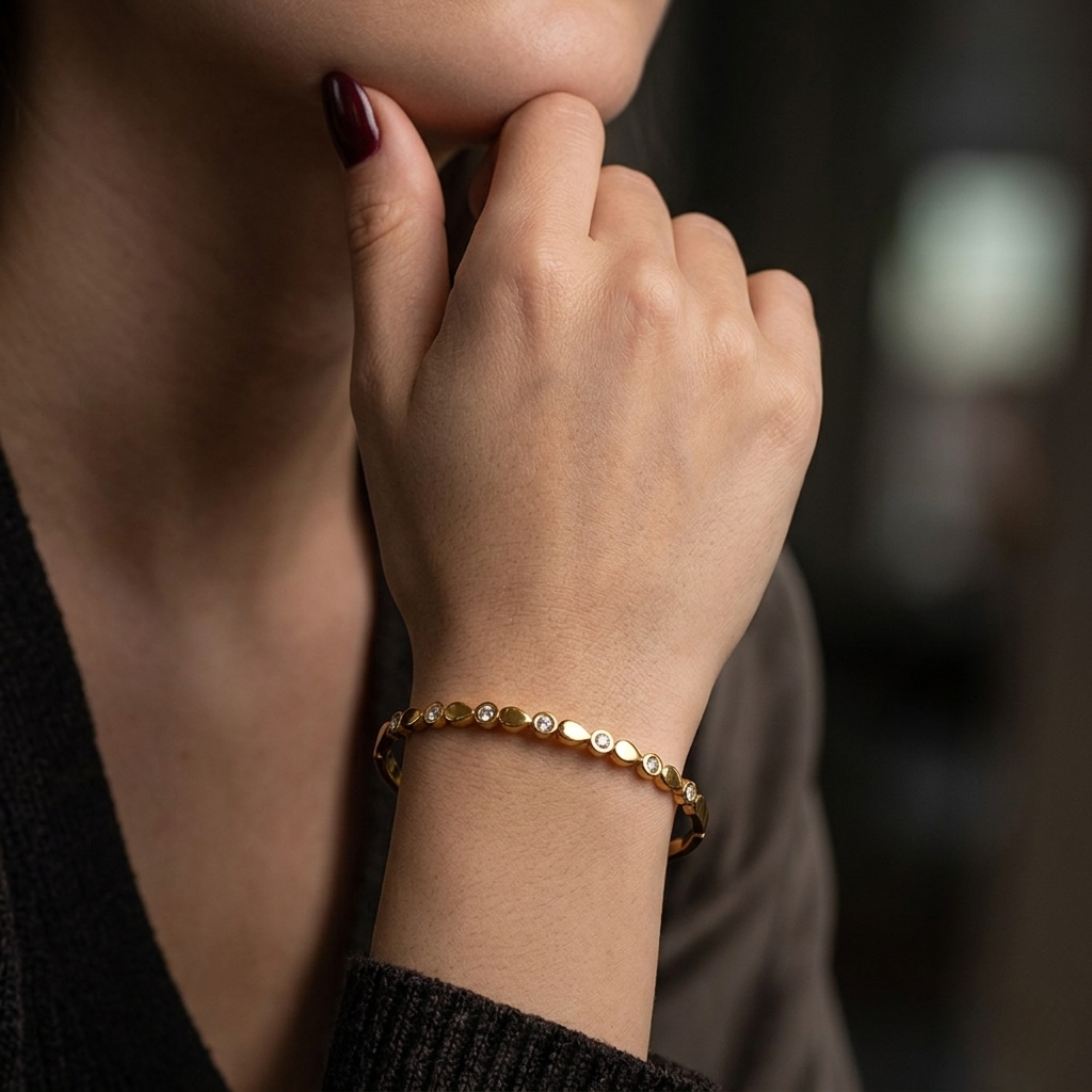 Gold modern link bangle on person's wrist with dark clothing background.