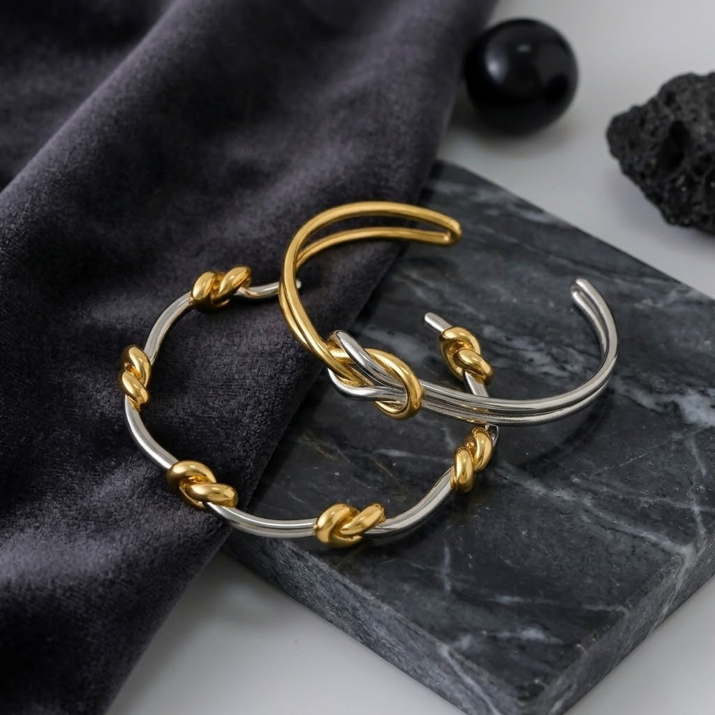 Duet Knot Bangle in silver and gold with knot details, placed on dark marble and velvet background.
