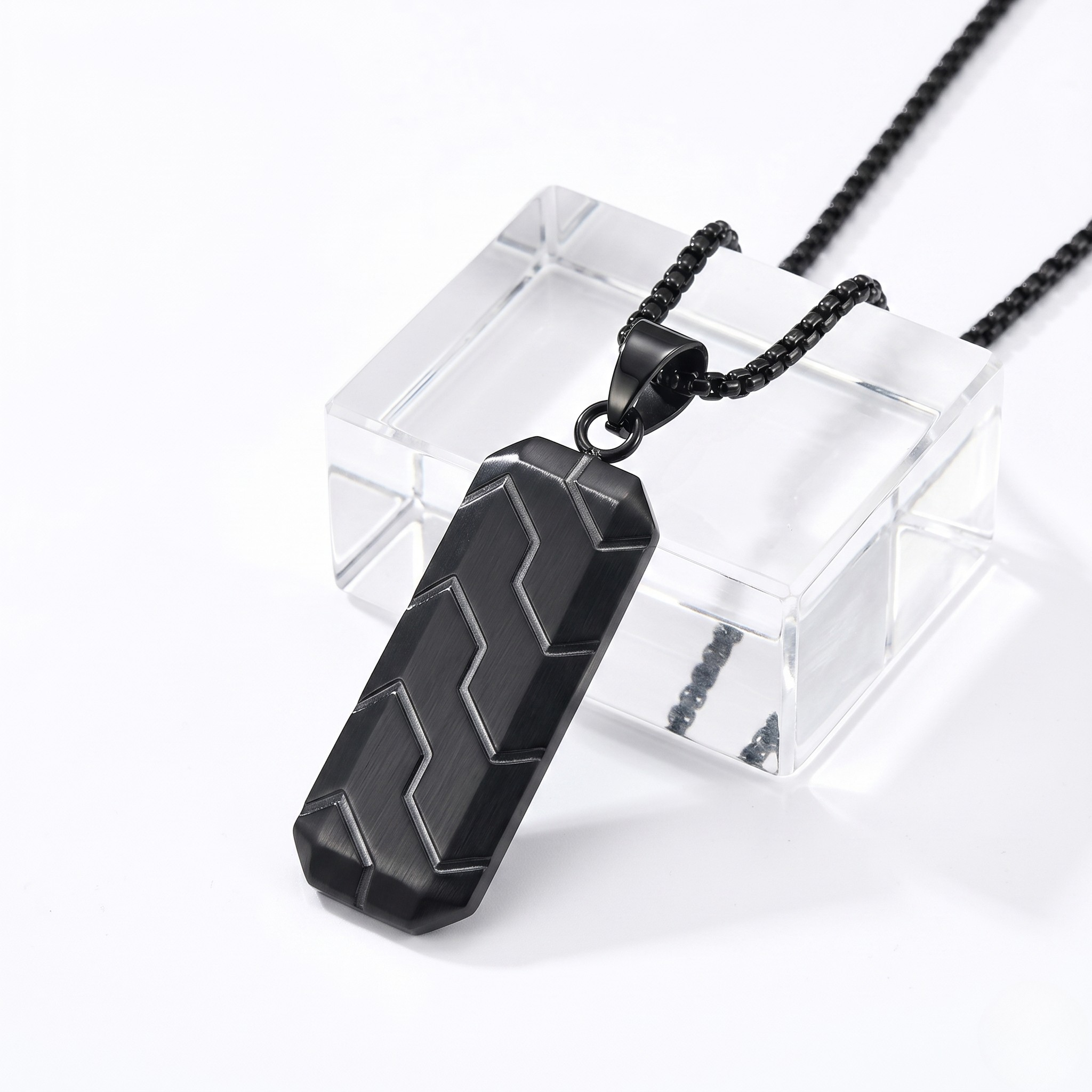 Black geometric pendant on chain with modern zigzag design, displayed on a clear stand.