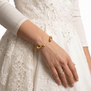 Gold plated cuff on a model's wrist, worn with an elegant lace dress.
