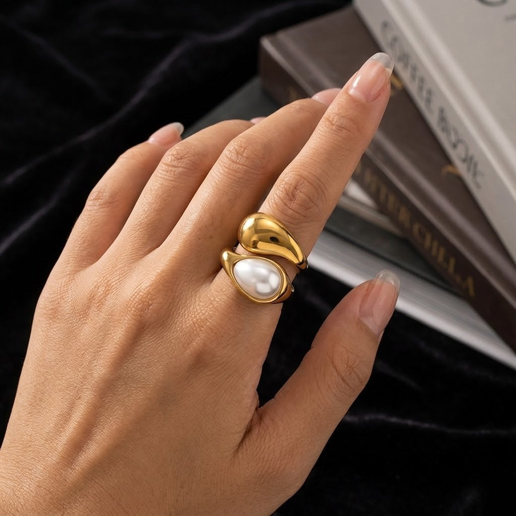 Gold-tone ring with pearl detail on a hand near books, showcasing J.Collins Jewelry's Polished Moonstone Ring.