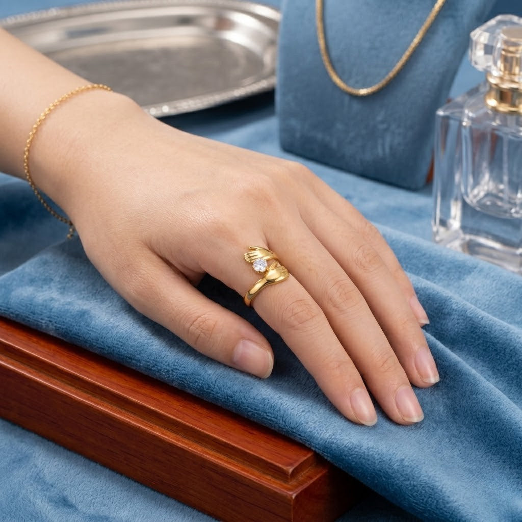 Gold embrace-style ring with a stone on a woman's hand, displayed on blue velvet with other jewelry items.